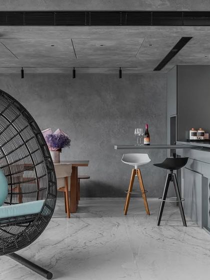 This living area showcases a confluence of concrete and color, reflecting a sophisticated yet approachable mindset. The design features a modern breakfast bar and a comfortable swing chair, creating distinct zones for different activities within an open, cohesive space.
