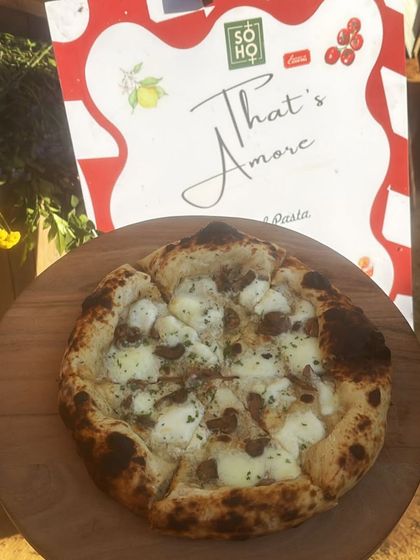 My Pizza al Tartufo, topped with earthy mushrooms and creamy cheese, sits on a wooden board in front of our "That's Amore" menu. It's a gourmet choice for truffle lovers.