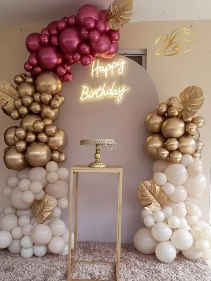 An elegant birthday setup with a beautiful balloon arch in white, gold, and magenta. The golden monstera leaf accents add a trendy, tropical touch to the decor.