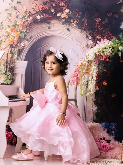 A little girl dressed in a pink princess gown, playing a miniature piano in a whimsical floral setting.