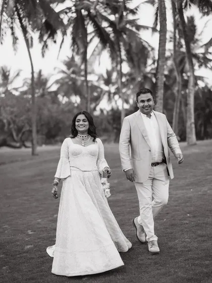 A classic black and white shot of a couple walking through the palm-fringed lawns of their Goa wedding venue.
