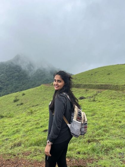 A smiling trekker on the trail, with the misty Kodachadri peaks in the background.