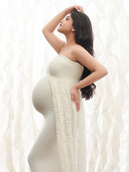 A powerful and graceful pose against a soft, white curtain backdrop. This high-key image beautifully showcases the silhouette of pregnancy in a simple, elegant style.