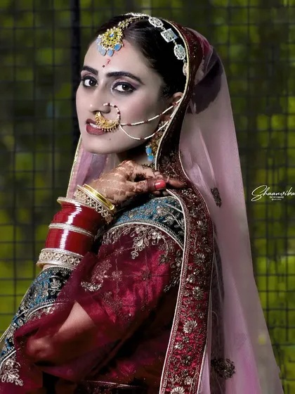A striking bridal portrait with dramatic lighting. The focus is on the bride's expressive eyes and the intricate details of her nath (nose ring) and other traditional jewelry.