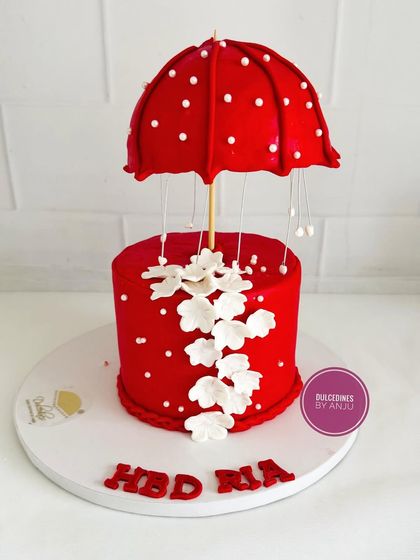 A whimsical red cake with an edible umbrella topper, with sugar "rain" dripping down onto fondant flowers.