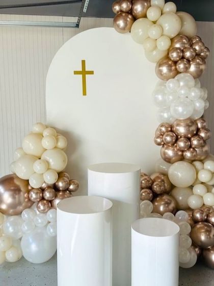 A simple and modern First Holy Communion balloon decoration. The clean white backdrop is accented with a cascade of beige and rose gold chrome balloons.