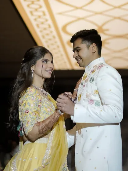 A sweet, interactive moment between the couple. Her makeup is fresh and bright, perfectly suited for a daytime engagement ceremony and complementing her colorful embroidered lehenga.