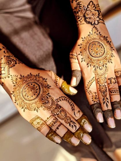This engagement mehendi features a central mandala on each palm, with delicate floral vines extending up the arms. The fingertips are kept dark for a traditional look.