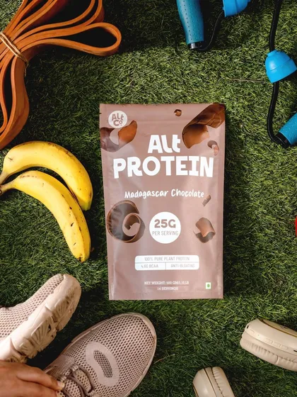 A flatlay of Alt Co. protein powder surrounded by workout gear. This composition directly targets the fitness community, positioning the product as an essential part of a workout routine.