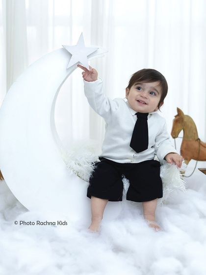 Reaching for the stars. A toddler enjoys our celestial moon theme, dressed in a smart little suit and sitting amongst fluffy clouds.