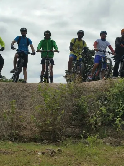 Riders silhouetted against the sky as they stand on a rock ledge with their bikes.