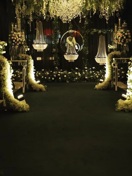 A detailed view of the enchanting reception entrance, focusing on the interplay of light, shadow, and texture from the hanging florals, chandeliers, and lush greenery.
