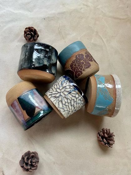 A collection of small tumblers made by students, showing off different carving and glazing techniques.