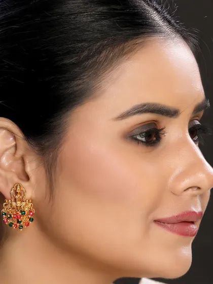 A close-up shot of a model wearing traditional temple earrings with multi-colored stones. The dark background makes the gold and gems stand out, perfect for high-impact product showcases.