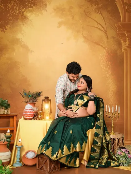 A culturally rich maternity session with a traditional Indian theme. The couple is posed against a painted backdrop depicting a classic scene, complete with props like lanterns and peacock feathers, creating a regal and unique portrait.