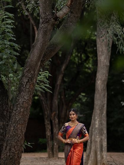 The model stands amidst the trees, the natural setting highlighting the earthy yet vibrant tones of her saree.