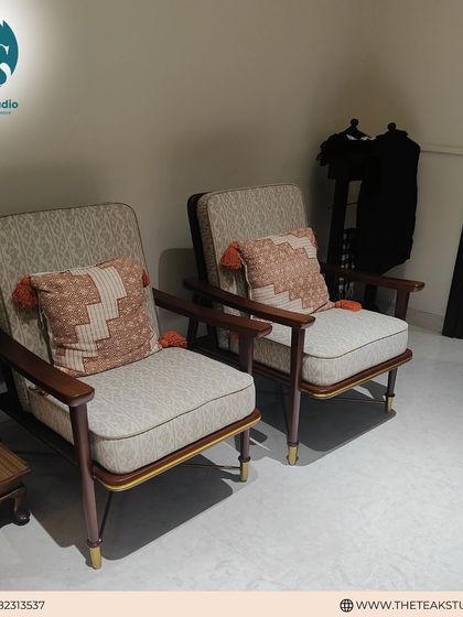 This pair of mid-century modern armchairs features a solid teakwood frame and comfortable upholstered cushions. The addition of patterned pillows with tassels adds a touch of bohemian flair.