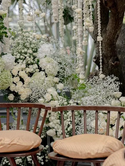 A close-up of the seating area at an all-white wedding, with chairs surrounded by lush floral installations.