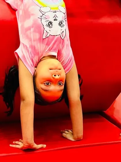 The pure joy of accomplishment. This close-up captures a young student's proud smile as she holds a handstand against a tumbler, a moment that perfectly represents the confidence boost our classes provide.