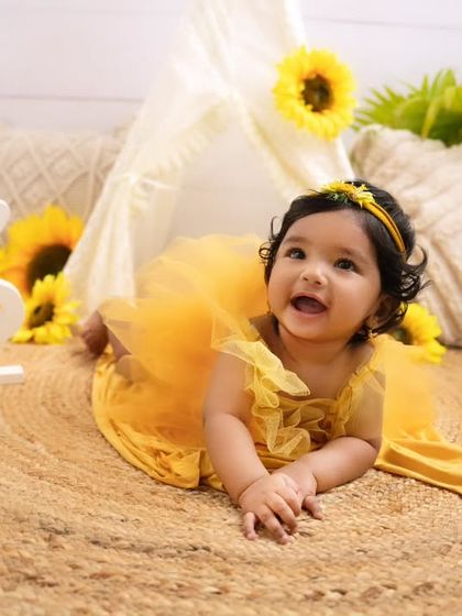 A happy baby girl enjoying tummy time on a jute rug during her sunflower-themed half-birthday shoot.