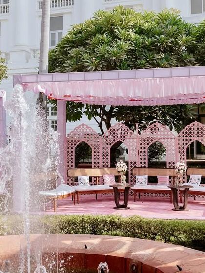 A whimsical Mehendi setup in the gardens of a heritage hotel. The space is defined by lavender canopies and intricate pink jaali panels, creating intimate and stylish seating areas for guests.