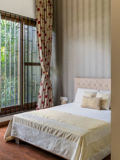 This bedroom showcases a more traditional aesthetic with a tufted headboard and classic patterned curtains. The large window, fitted with a security grille, looks out onto a garden, bringing a sense of nature and security into the tranquil space.