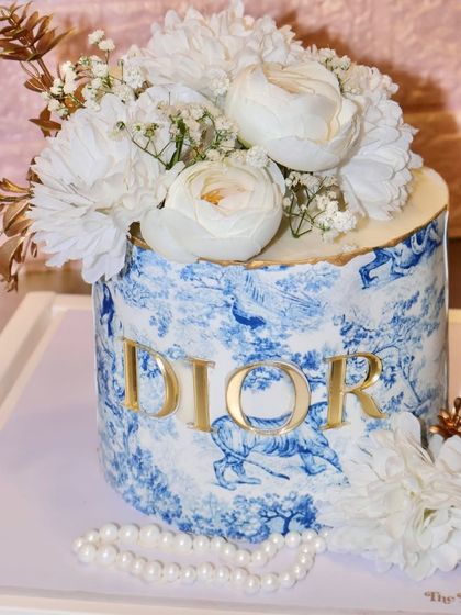 A little Dior, a lot of allure. This stunning cake features the iconic blue and white Dior print, a gold logo, and is topped with a bouquet of fresh white flowers.