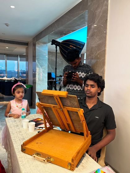 A behind-the-scenes shot of me sketching a young girl, with a photographer capturing the moment.