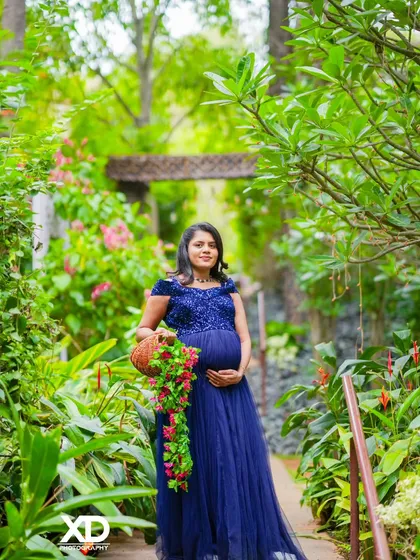 A beautiful solo portrait of the mother-to-be in a blue gown, holding a basket of flowers in a lush garden path.