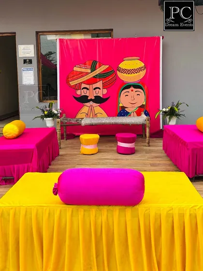 A quirky and traditional Haldi seating area. I used a fun, illustrated backdrop with bright pink and yellow seating to create a playful and memorable setup.