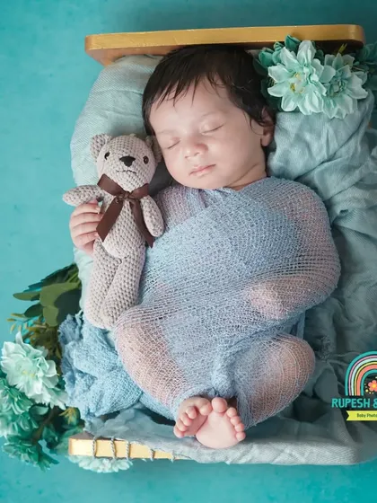 A newborn wrapped in blue, cuddling a small teddy bear. This classic pose emphasizes the baby's small size and peaceful nature.