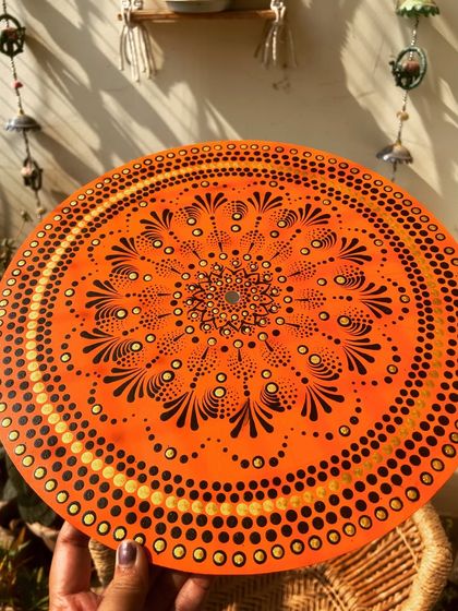A finished dot mandala in a warm orange and black color scheme, glowing in the sunlight.