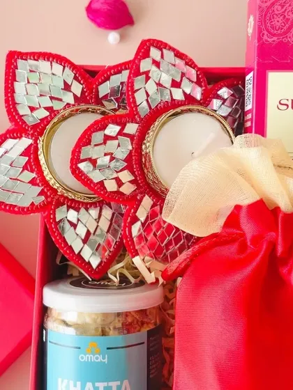 A close-up of the red Diwali box, focusing on the vibrant mirror-work T-light holder and the jar of Khatta Meetha snack mix.