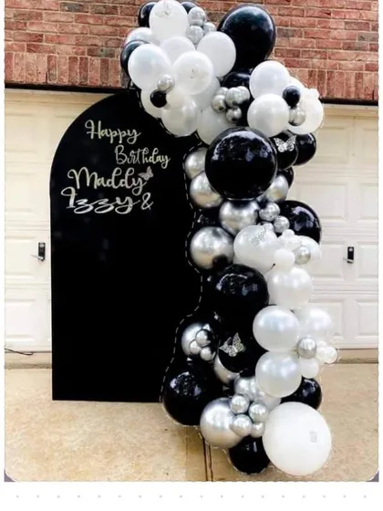 A stylish black, white, and silver balloon garland on a black arched backdrop, personalized for a joint birthday celebration.