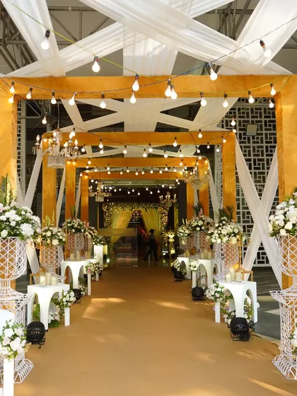 This bright and airy entrance features a mustard-yellow frame with white drapes and string lights, perfect for a daytime wedding or a vibrant Mehendi ceremony.