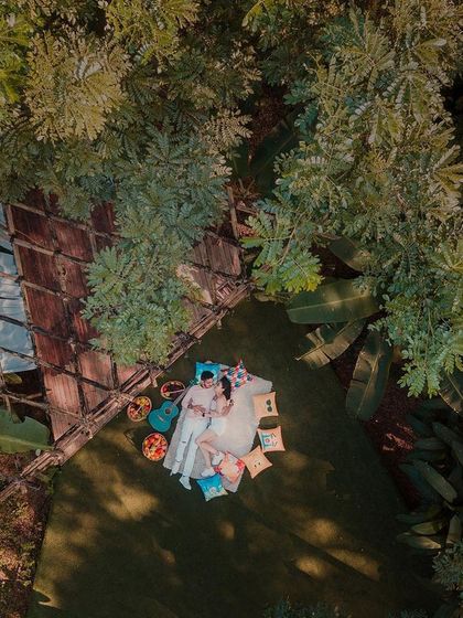 A bird's-eye view of a perfect afternoon. This drone shot captures a couple enjoying a romantic picnic, nestled in a clearing surrounded by lush greenery, creating a feeling of a private, hidden paradise.