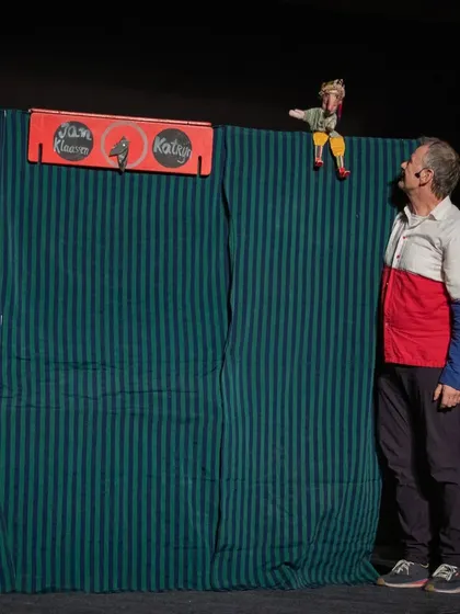 The puppeteer looks up at his own creation, Jan Klaassen, who sits atop the puppet booth, breaking the fourth wall in a comedic way.
