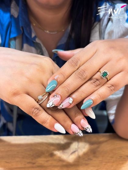 A creative mix of styles on almond-shaped nails, combining solid teal, a classic white French tip, and intricate black and white floral line art for a modern, artistic manicure.