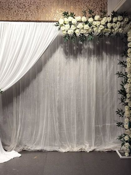 A simple and elegant backdrop option using an L-shaped frame of white roses against a sheer white curtain. This is a versatile setup for any pre-wedding function.
