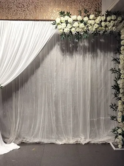 A simple and elegant backdrop option using an L-shaped frame of white roses against a sheer white curtain. This is a versatile setup for any pre-wedding function.