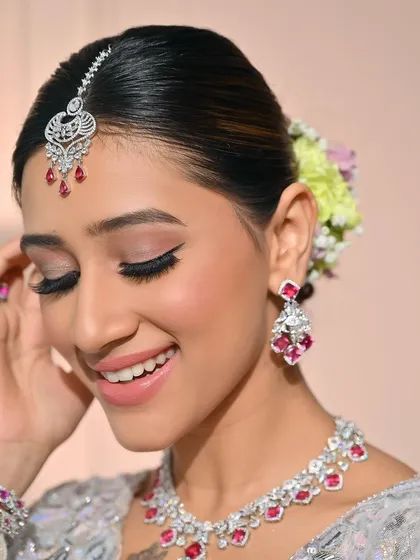 A happy, smiling close-up that shows off the delicate eye makeup and radiant skin. The pop of ruby in the jewelry is beautifully complemented by the soft pink tones in the makeup.