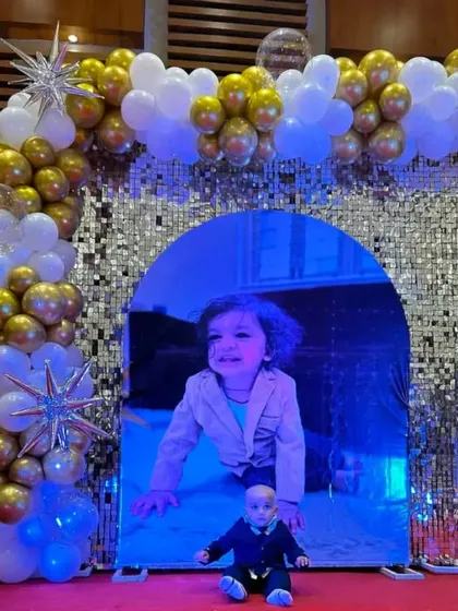 A unique birthday backdrop with a mirrored archway set against a silver sequin wall. The setup is framed by a white and gold balloon garland, creating a cool, reflective photo spot.