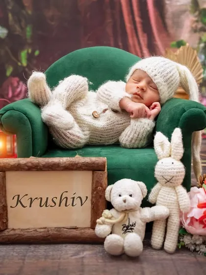 A personalized newborn setup with baby Krushiv sleeping in a bunny outfit on a miniature sofa.