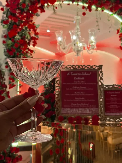 A guest's perspective, holding a beautiful crystal coupe glass against the backdrop of our elegantly decorated bar. This image captures the sophisticated and personal experience we aim to create at every event.