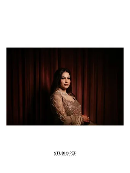 A simple, elegant portrait of Nisha against a dark curtain, the lighting focused on her, creating a classic and timeless look.