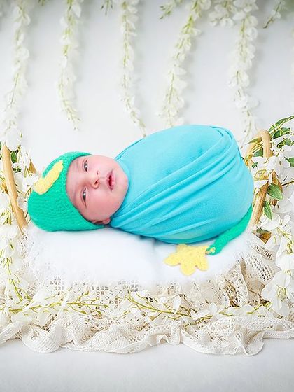 A dreamy, whimsical shot with a baby in a frog-themed hat, resting on a swing adorned with beautiful white lace and flowers.