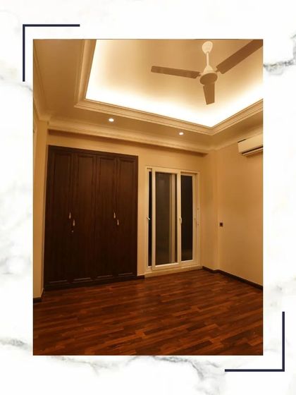 This bedroom features a dark wood, floor-to-ceiling wardrobe that provides a rich contrast to the light walls. The wooden flooring and clean false ceiling complete the elegant and cohesive design.