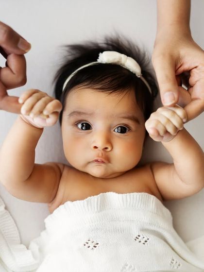 Look at this adorable four-month-old! Those big, curious eyes and tiny hands holding onto her parents' fingers are just too sweet.