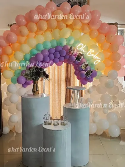 Celebrating a new arrival with a soft and sweet pastel rainbow baby shower theme. This setup features a beautiful balloon arch in rainbow colors, cloud-like white balloons, and an 'Oh Baby' neon sign. The three pedestals are ready for the cake and gifts.