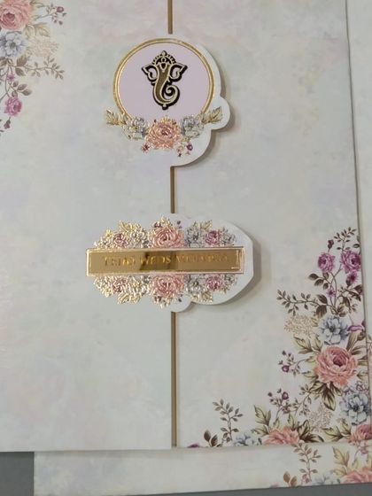 A beautiful gate-fold invitation with a floral design and two golden emblems, one featuring Ganesha. This card perfectly blends auspicious symbols with soft, romantic florals.